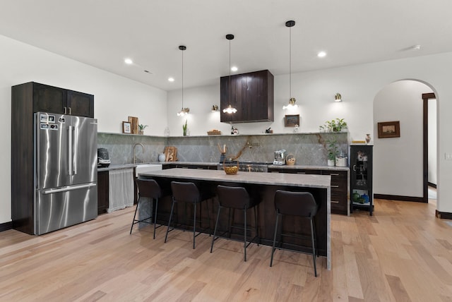7617 S Cedar Rd, Spokane, WA 99224 - kitchen featuring freestanding refrigerator, arched walkways, light wood-style flooring, tasteful backsplash, and a kitchen bar
