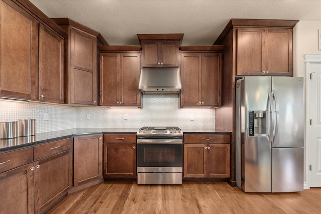 9302 W Floyd Dr, Cheney, WA 99004 - kitchen with appliances with stainless steel finishes, exhaust hood, light wood-type flooring, tasteful backsplash, and dark stone counters