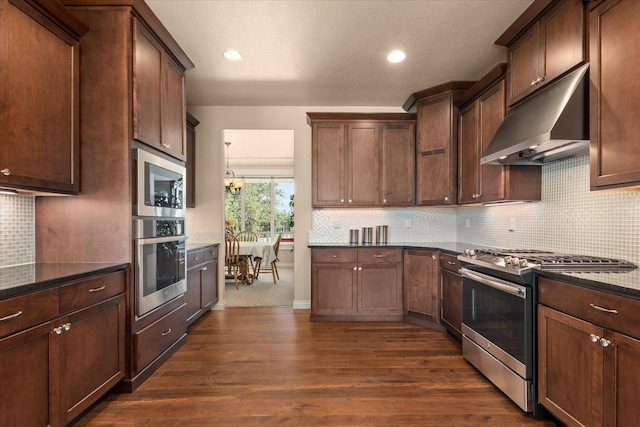9302 W Floyd Dr, Cheney, WA 99004 - kitchen with stainless steel appliances, under cabinet range hood, dark stone counters, tasteful backsplash, and dark wood-type flooring