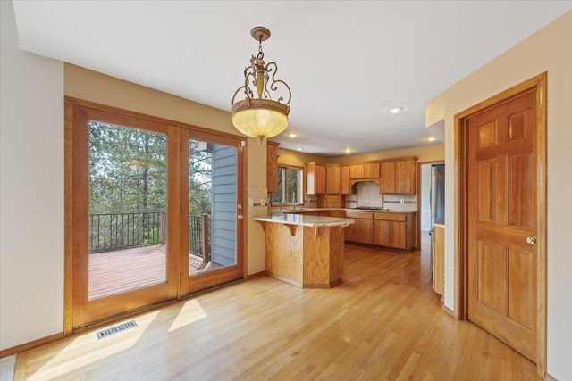 15116 N Edencrest Dr, Spokane, WA 99208 - kitchen featuring a peninsula, light wood-type flooring, light countertops, brown cabinetry, and tasteful backsplash