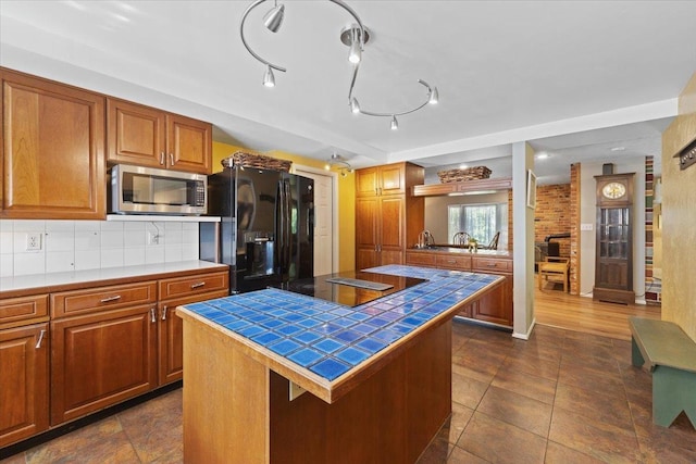 3410 S Napa St, Spokane, WA 99203 - kitchen featuring stainless steel microwave, tile countertops, black refrigerator with ice dispenser, brown cabinets, and backsplash