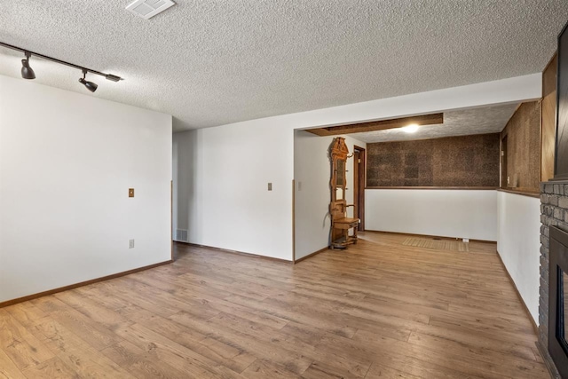 14417 N Dakota Rd, Spokane, WA 99208 - empty room featuring a textured ceiling, a brick fireplace, light wood-type flooring, and rail lighting