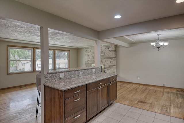 9405 N Normandie Ln, Spokane, WA 99218 - kitchen with a chandelier, a textured ceiling, a kitchen breakfast bar, light tile patterned flooring, and light stone counters