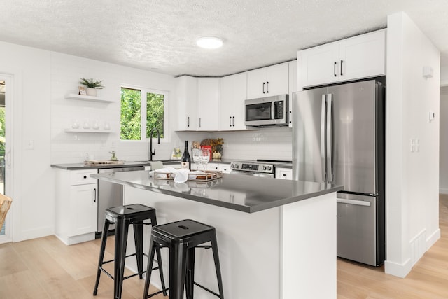 7721 N Wilding Dr, Spokane, WA 99208 - kitchen featuring appliances with stainless steel finishes, open shelves, light wood-style floors, a breakfast bar, and a textured ceiling