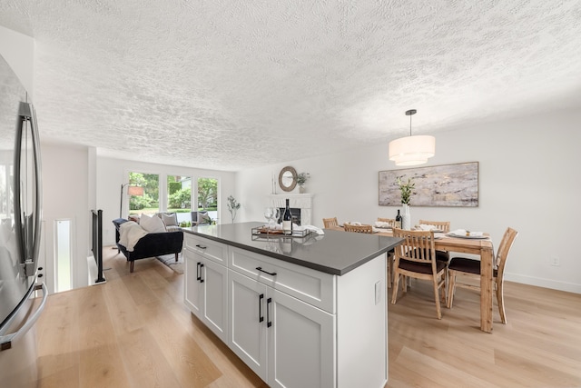 7721 N Wilding Dr, Spokane, WA 99208 - kitchen with a textured ceiling, dark countertops, light wood-style floors, stainless steel fridge, and a center island