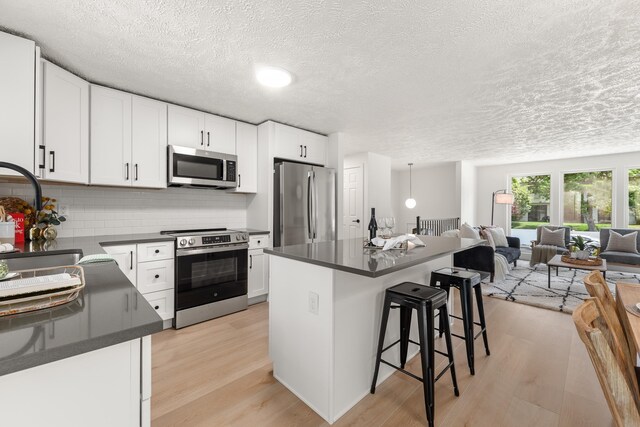 7721 N Wilding Dr, Spokane, WA 99208 - kitchen with stainless steel appliances, dark countertops, light wood-style floors, open floor plan, and a textured ceiling