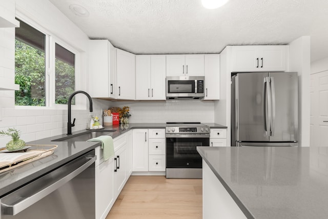 7721 N Wilding Dr, Spokane, WA 99208 - kitchen featuring appliances with stainless steel finishes, white cabinets, a textured ceiling, backsplash, and light wood-type flooring