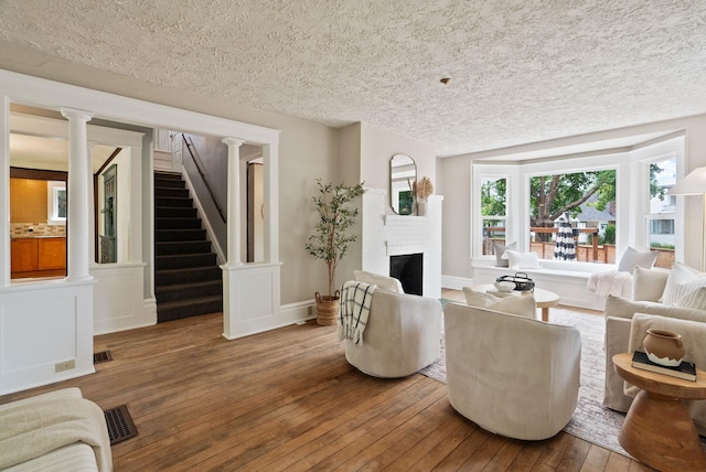 1315 N Hollis St, Spokane, WA 99201 - living area featuring hardwood / wood-style floors, a textured ceiling, a fireplace, stairs, and decorative columns