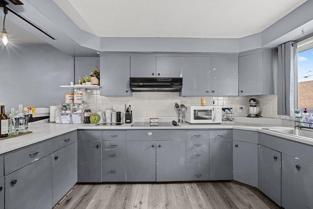 1630 E Broad Ave, Spokane, WA 99207 - kitchen with gray cabinets, under cabinet range hood, white microwave, light wood-style floors, and tasteful backsplash