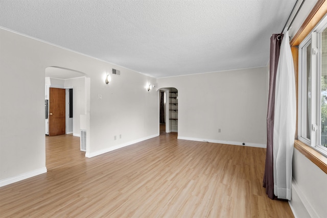 3918 E 8th Ave, Spokane, WA 99202 - spare room featuring arched walkways, light wood-style flooring, a textured ceiling, and ornamental molding