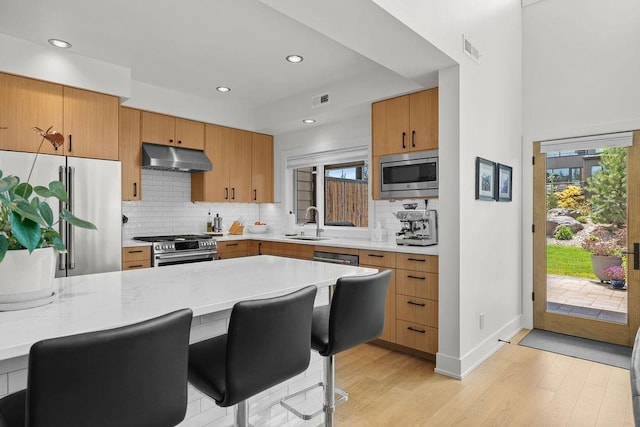 4408 E 23rd Ln, Spokane, WA 99223 - kitchen with appliances with stainless steel finishes, under cabinet range hood, light wood finished floors, tasteful backsplash, and recessed lighting