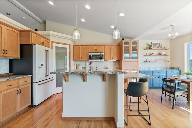 711 W Bolan Ave, Spokane, WA 99224 - kitchen featuring white refrigerator with ice dispenser, stainless steel microwave, vaulted ceiling, tasteful backsplash, and a kitchen bar