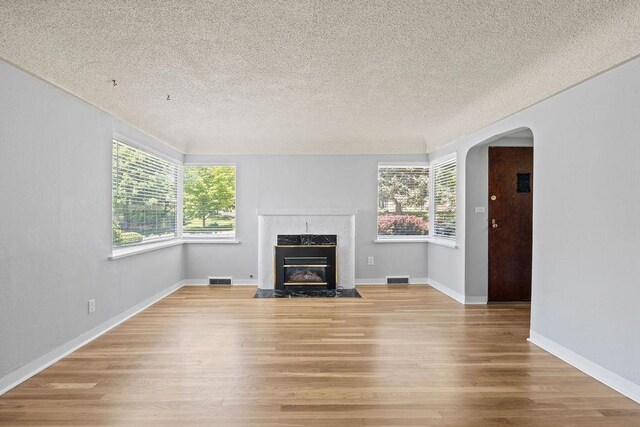 3307 W Euclid Ave, Spokane, WA 99205 - unfurnished living room featuring a textured ceiling, plenty of natural light, light wood-style flooring, arched walkways, and a fireplace