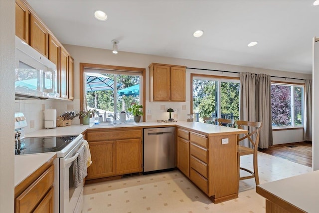 4108 S Greystone Ln, Spokane, WA 99223 - kitchen featuring white appliances, a peninsula, decorative backsplash, light countertops, and a kitchen bar