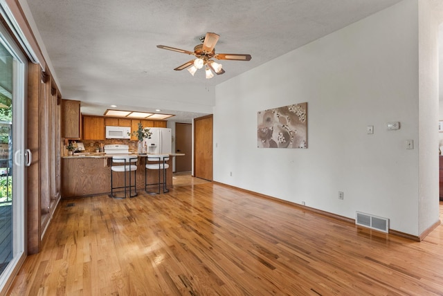 3827 E Funk Ave, Spokane, WA 99223 - kitchen with brown cabinets, white appliances, a peninsula, light wood finished floors, and a textured ceiling