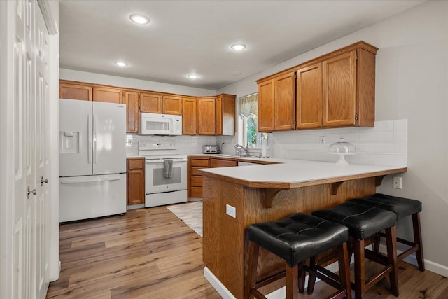 6310 W Sundance Dr, Spokane, WA 99208 - kitchen featuring white appliances, brown cabinetry, a peninsula, light wood-style flooring, and decorative backsplash