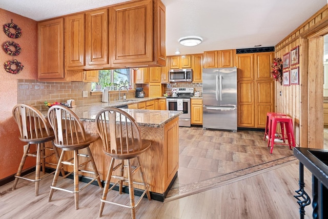 3425 E Upriver Dr, Spokane, WA 99217 - kitchen featuring appliances with stainless steel finishes, a peninsula, backsplash, light stone countertops, and light wood-style flooring