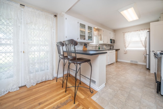 5224 N Post St, Spokane, WA 99204 - kitchen with stainless steel appliances, dark countertops, white cabinetry, a peninsula, and glass insert cabinets