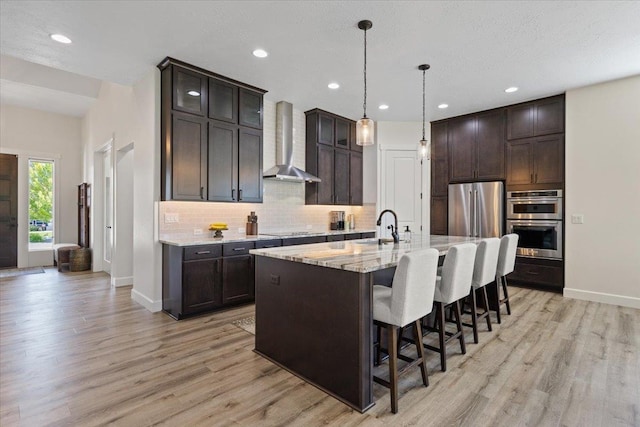 12918 E San Juan Ln, Spokane, WA 99206 - kitchen with wall chimney range hood, stainless steel appliances, light wood finished floors, tasteful backsplash, and a kitchen bar