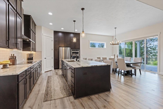 12918 E San Juan Ln, Spokane, WA 99206 - kitchen with light wood-style floors, dark brown cabinets, black electric stovetop, tasteful backsplash, and freestanding refrigerator