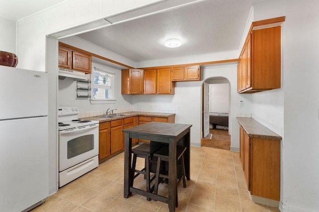 1019 E Everett Ave, Spokane, WA 99207 - kitchen featuring white appliances, under cabinet range hood, brown cabinetry, and arched walkways
