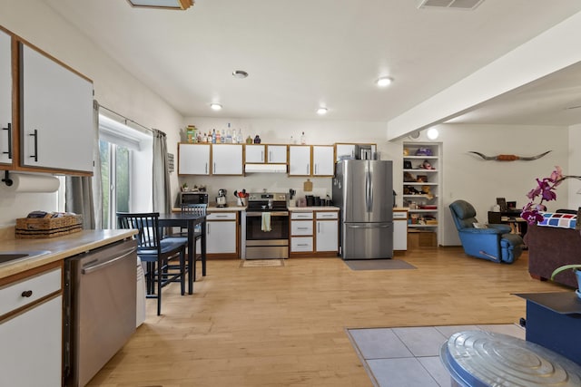 20902 S Ritchey Rd, Spokane, WA 99004 - kitchen with stainless steel appliances, under cabinet range hood, light wood-type flooring, light countertops, and white cabinets