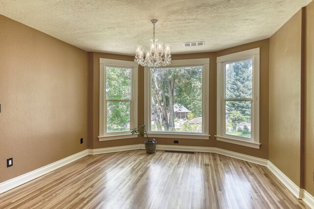1428 E 18th Ave, Spokane, WA 99203 - unfurnished dining area with wood finished floors, a chandelier, healthy amount of natural light, a textured ceiling, and a textured wall
