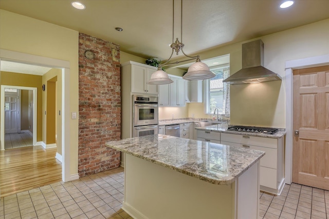 1428 E 18th Ave, Spokane, WA 99203 - kitchen featuring wall chimney range hood, appliances with stainless steel finishes, a kitchen island, white cabinetry, and light tile patterned flooring