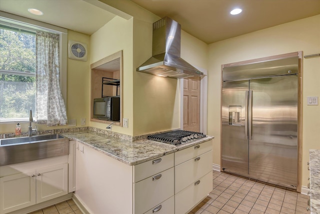 1428 E 18th Ave, Spokane, WA 99203 - kitchen with stainless steel appliances, wall chimney exhaust hood, white cabinetry, light tile patterned flooring, and light stone counters