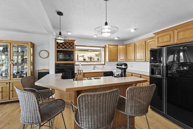 17607 E Judkins Rd, Spokane, WA 99217 - kitchen featuring black appliances, light wood-type flooring, a textured ceiling, a kitchen island, and a breakfast bar area