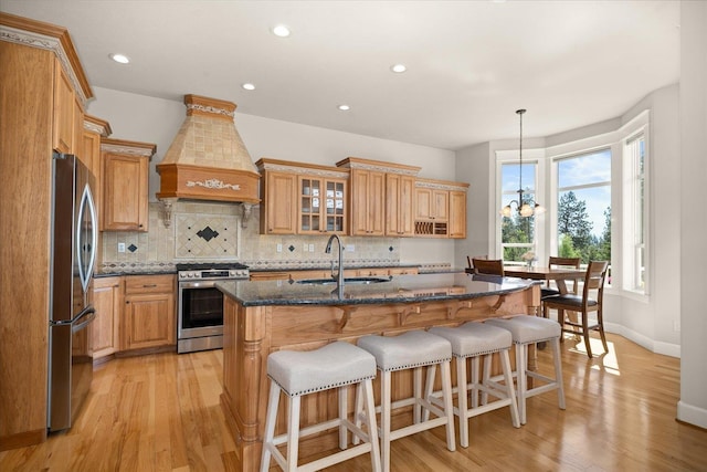 5614 N Thierman Rd, Spokane, WA 99217 - kitchen with stainless steel appliances, premium range hood, light wood-style floors, tasteful backsplash, and a center island with sink