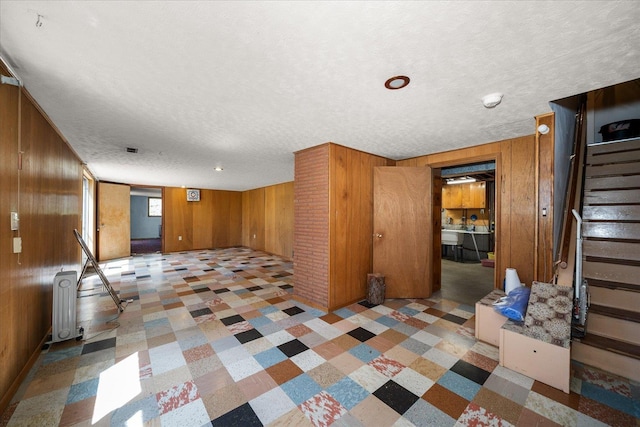 11322 E 18th Ave, Spokane, WA 99206 - unfurnished living room featuring radiator, tile patterned floors, wood walls, stairway, and a textured ceiling