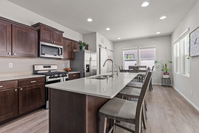 1225 E Paske Rd, Colbert, WA 99005 - kitchen featuring stainless steel appliances, a barn door, a breakfast bar area, light wood-type flooring, and an island with sink