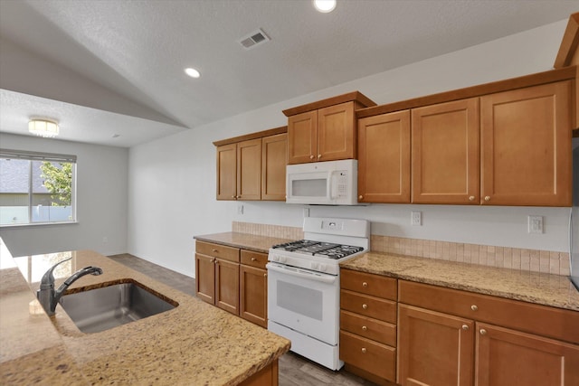 8812 W Pirates Ct, Spokane, WA 99224 - kitchen with white appliances, brown cabinets, vaulted ceiling, light stone countertops, and recessed lighting