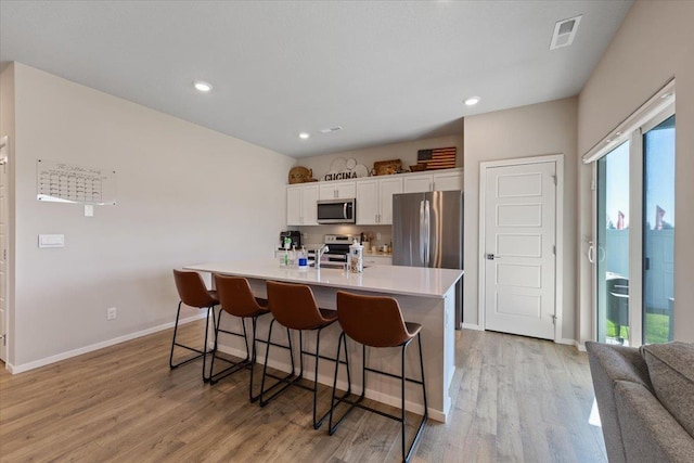 8403 W Red Ave, Cheney, WA 99004 - kitchen with stainless steel appliances, white cabinets, a kitchen breakfast bar, light countertops, and light wood-style flooring