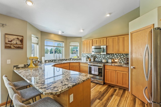 12837 E 37th Ln, Spokane Valley, WA 99206 - kitchen with appliances with stainless steel finishes, a peninsula, a kitchen bar, light wood finished floors, and tasteful backsplash