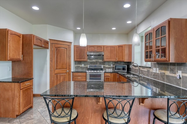 7302 N Quamish Dr, Spokane, WA 99208 - kitchen featuring stainless steel appliances, brown cabinets, a peninsula, dark stone counters, and glass insert cabinets