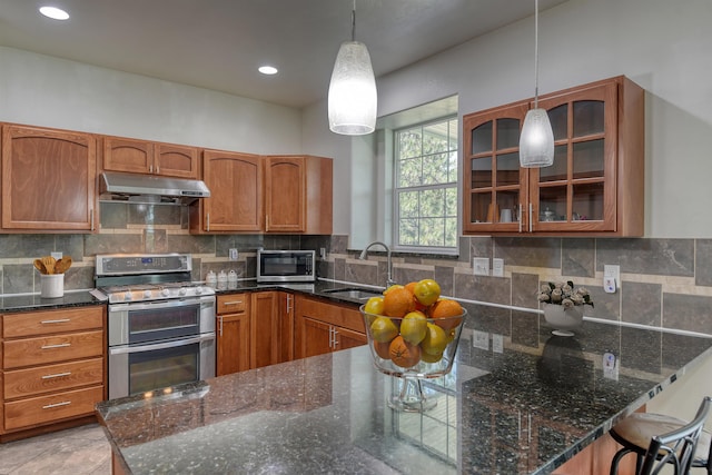 7302 N Quamish Dr, Spokane, WA 99208 - kitchen with under cabinet range hood, stainless steel appliances, glass insert cabinets, brown cabinetry, and recessed lighting