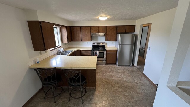 3520 N Arden Rd, Otis Orchards, WA 99027 - kitchen with stainless steel appliances, under cabinet range hood, light countertops, dark brown cabinetry, and a peninsula