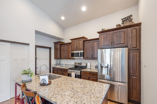 3316 N Coleman St, Post Falls, ID 83854 - kitchen with appliances with stainless steel finishes, dark brown cabinets, light stone countertops, a center island with sink, and light wood-type flooring