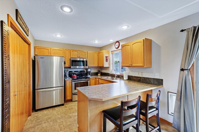 11606 E 8th Ave, Spokane Valley, WA 99206 - kitchen with stainless steel appliances, a peninsula, light brown cabinetry, a kitchen bar, and recessed lighting