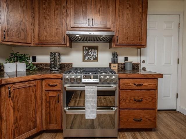 10108 E 19th Ave, Spokane Valley, WA 99206 - kitchen with range with two ovens, under cabinet range hood, light wood-style floors, dark countertops, and brown cabinets