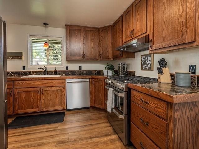 10108 E 19th Ave, Spokane Valley, WA 99206 - kitchen featuring appliances with stainless steel finishes, under cabinet range hood, dark countertops, brown cabinetry, and light wood-type flooring