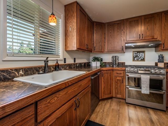 10108 E 19th Ave, Spokane Valley, WA 99206 - kitchen featuring appliances with stainless steel finishes, under cabinet range hood, dark countertops, and light wood-style floors