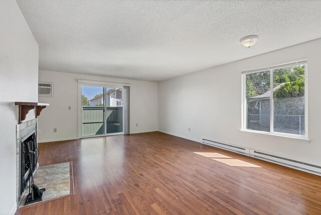 6125 N Addison St, Spokane, WA 99208 - unfurnished living room with baseboard heating, wood finished floors, a textured ceiling, a wall mounted air conditioner, and a fireplace with flush hearth