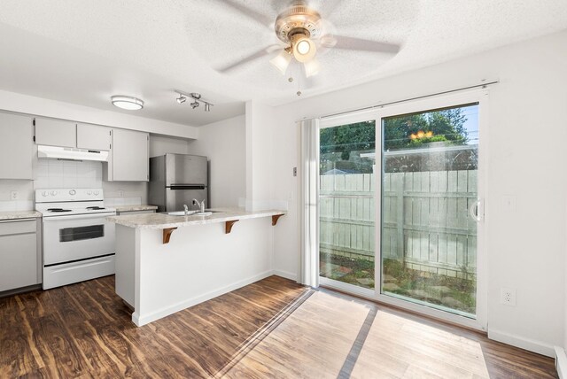 6125 N Addison St, Spokane, WA 99208 - kitchen featuring white range with electric cooktop, under cabinet range hood, freestanding refrigerator, a peninsula, and light countertops