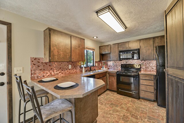 4232 E 10th Ave, Spokane, WA 99202 - kitchen with black appliances, a peninsula, decorative backsplash, a textured ceiling, and a breakfast bar