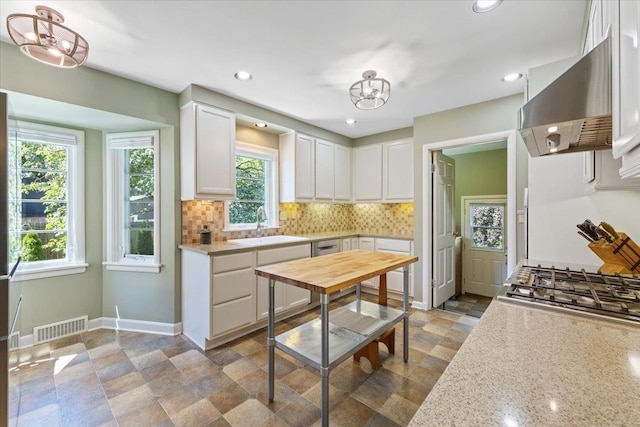 2718 S Hatch St, Spokane, WA 99203 - kitchen with wall chimney range hood, white cabinetry, a chandelier, decorative backsplash, and stone finish floors