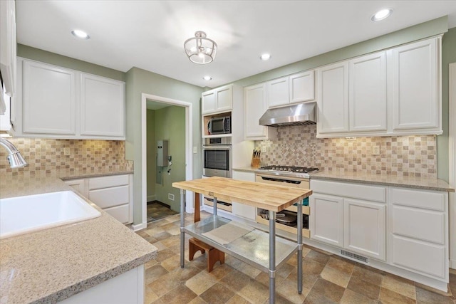 2718 S Hatch St, Spokane, WA 99203 - kitchen with stainless steel microwave, under cabinet range hood, white cabinets, stone finish floors, and recessed lighting