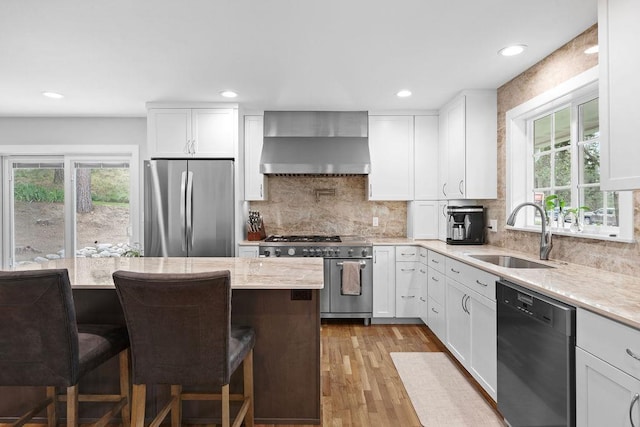 3929 S Best Ct, Veradale, WA 99037 - kitchen featuring appliances with stainless steel finishes, wall chimney exhaust hood, light wood-style flooring, light stone counters, and a breakfast bar area